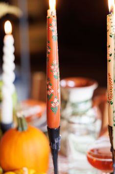 two candles are sitting on a table with oranges and pumpkins in the background