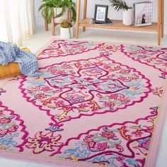 a pink area rug with an ornate design on the center and bottom, in front of a window