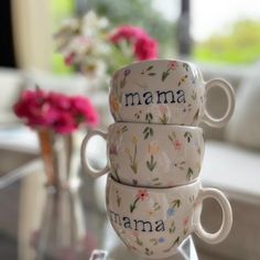 three coffee cups sitting on top of a glass table next to pink and white flowers