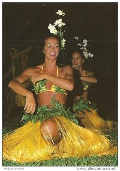 two women in yellow hula skirts sitting on the grass with flowers around their necks