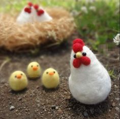 three little chickens are sitting in the dirt next to some grass and flowers, one is white with red on it's head