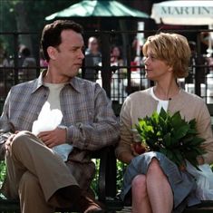 a man and woman sitting on a park bench with flowers in their hands, looking at each other