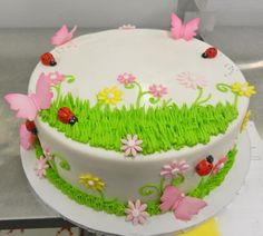 a cake decorated with grass, flowers and ladybugs