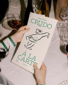 a person is holding up a book at a table with wine glasses and plates on it