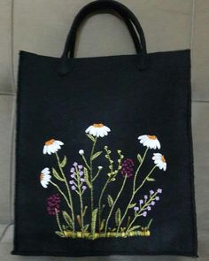 a black bag with white daisies and purple flowers embroidered on the front, sitting on a tile floor