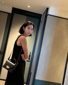 a woman standing in front of a mirror holding a black purse and looking at her reflection