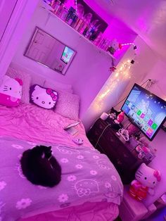 a black cat laying on top of a bed next to a tv and pink comforter