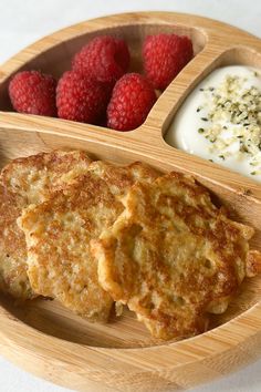 a wooden plate topped with pancakes next to raspberries and yogurt sauce