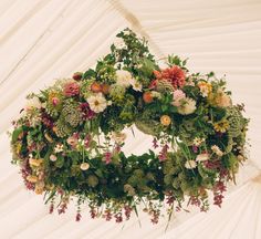 a floral wreath hanging from the ceiling in a white tent with flowers and greenery