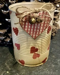 a tin can with a heart on it and some pine cones in the back ground