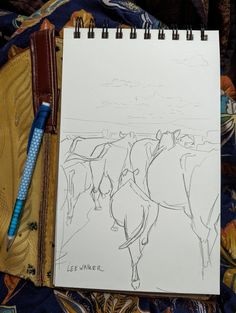 a drawing of horses is shown next to a pen and notebook on a bed sheet