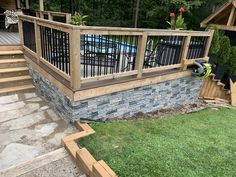 a wooden deck with black iron railings and stone steps leading up to a swimming pool