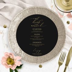 a black and gold wedding menu on a white plate with pink flowers next to it