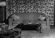 an old black and white photo of a living room with couches, coffee table and curtains