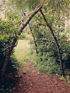 a wooden arch made out of branches in the middle of a garden with grass and trees