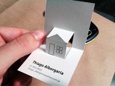 a person holding up a business card with a house cut out on it's front