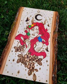 a piece of wood with an image of a mermaid on it sitting in the grass