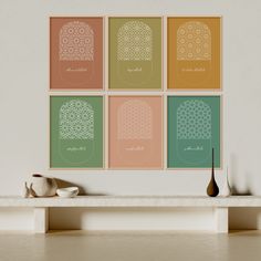 four framed art prints on a wall above a table with vases and other items