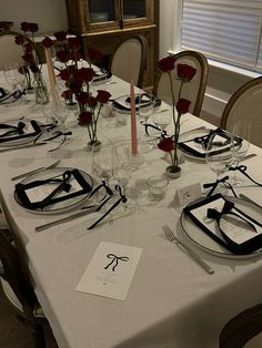 the table is set with place settings and flowers in vases on each side, along with silverware