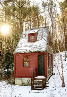 a small red cabin in the woods with snow on the ground and stairs leading up to it