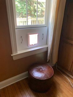 a brown ottoman sitting in front of a window next to a wooden floor and door