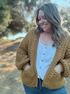 a woman is smiling while wearing a cardigan sweater and jeans with her hands on her hips