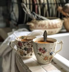 two coffee cups with spoons in them sitting on a counter