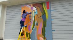 a man is painting on the side of a building with colorful paint and ladders