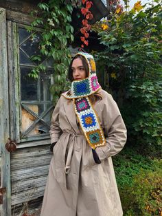 a woman standing in front of an old building wearing a crocheted granny hat and scarf