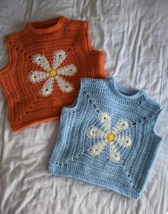 two crocheted sweaters laying on top of a white bed next to each other