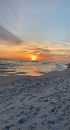 the sun is setting at the beach with footprints in the sand