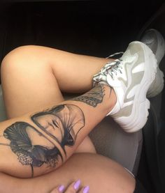 a woman with tattoos on her legs laying in the back seat of a car next to a white shoe