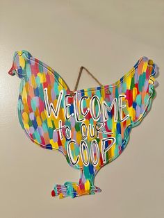 a welcome sign hanging from the side of a wall with an image of a chicken painted on it