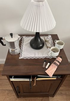 a table with a lamp, coffee mugs and other items on top of it