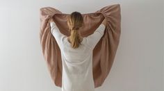 a woman standing in front of a white wall covering her back with a brown blanket