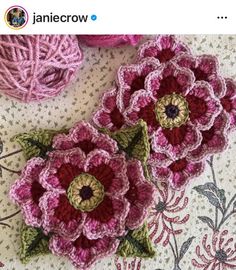 two crocheted flowers sitting on top of a table next to balls of yarn