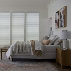 a bed sitting in a bedroom next to two windows with blind shades on the windows