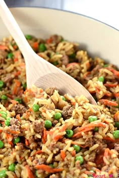 a pot filled with rice, peas and ground beef next to a wooden spatula