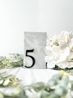 a marble block with the number five on it next to white flowers and greenery