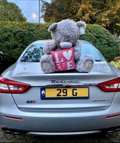 a teddy bear sitting on the hood of a car