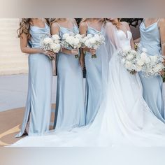 a group of women standing next to each other wearing blue dresses and holding bouquets