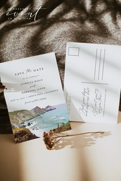 two wedding cards sitting on top of a bed next to an envelope with the word save the date written on it