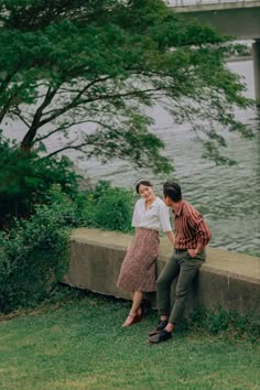 a man and woman sitting next to each other on the side of a riverbank