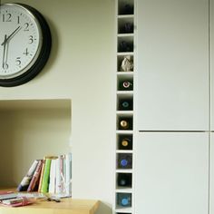 a clock on the wall next to a book shelf with books and magazines in it