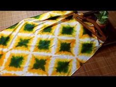 a yellow and green tie - dyed blanket sitting on top of a wooden table next to a potted plant