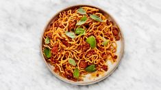 a plate full of spaghetti with basil leaves on top and meat sauce in the middle