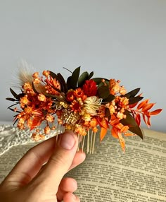 a hand holding a hair comb with flowers on top of an open book in front of a gray wall