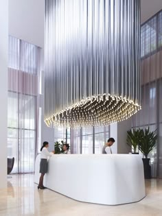 two people are standing in front of a reception counter with lights hanging from the ceiling