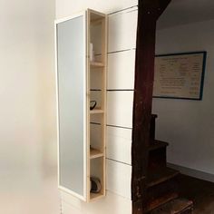 an open cabinet sitting on the side of a white wall next to a wooden step