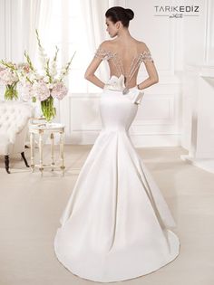 a woman in a white dress standing next to a table with flowers on it and the back of her dress is open